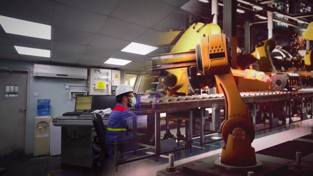 Operador frente a pantallas de control industrial y brazos robóticos soldando en una línea automatizada