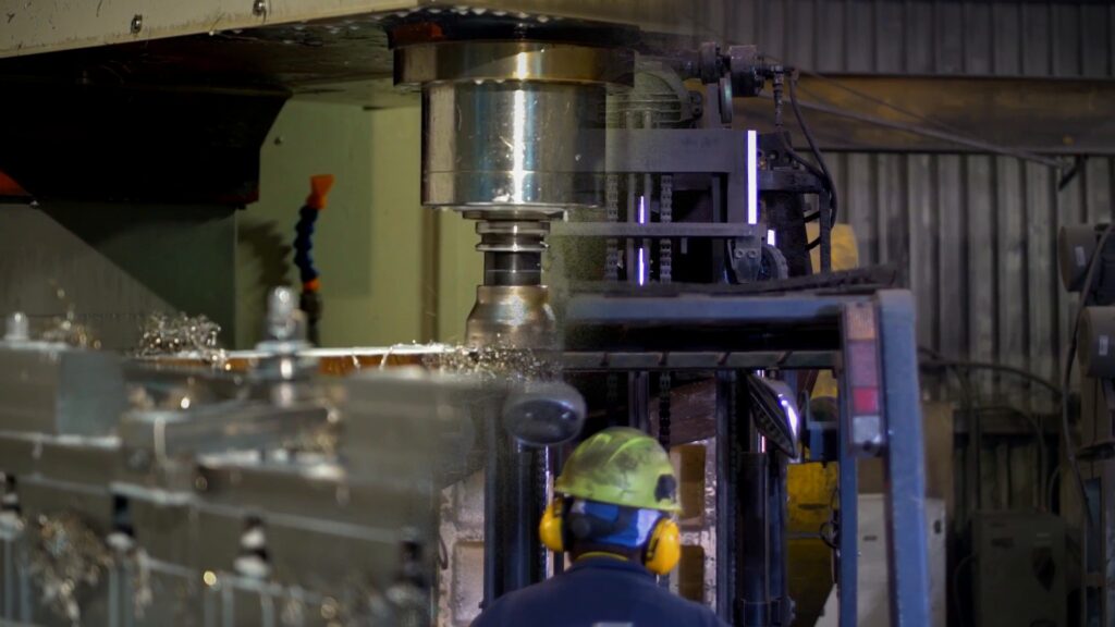 Fresadora CNC cortando metal y montacargas trabajando en una planta de manufactura
