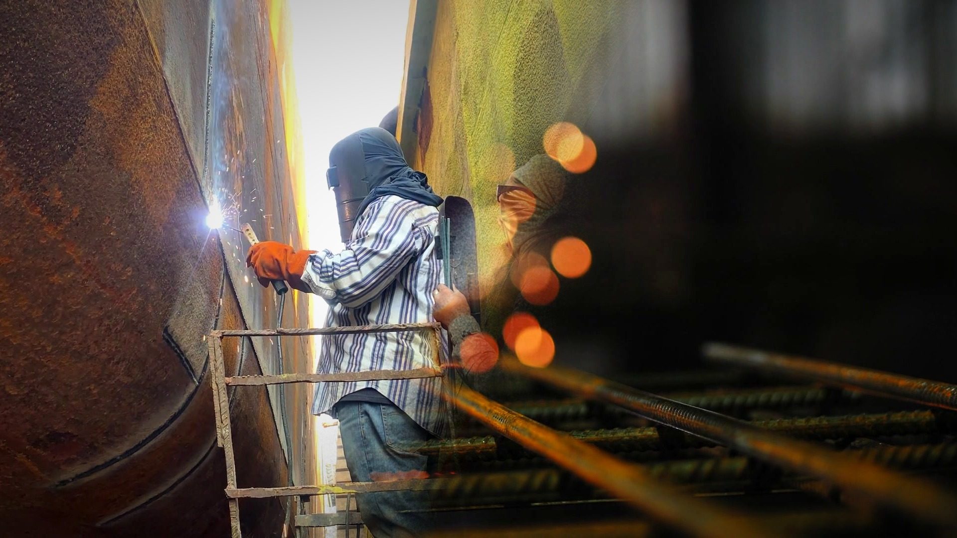 Soldador con careta trabaja junto a un brazo extractor de humos en una nave industrial